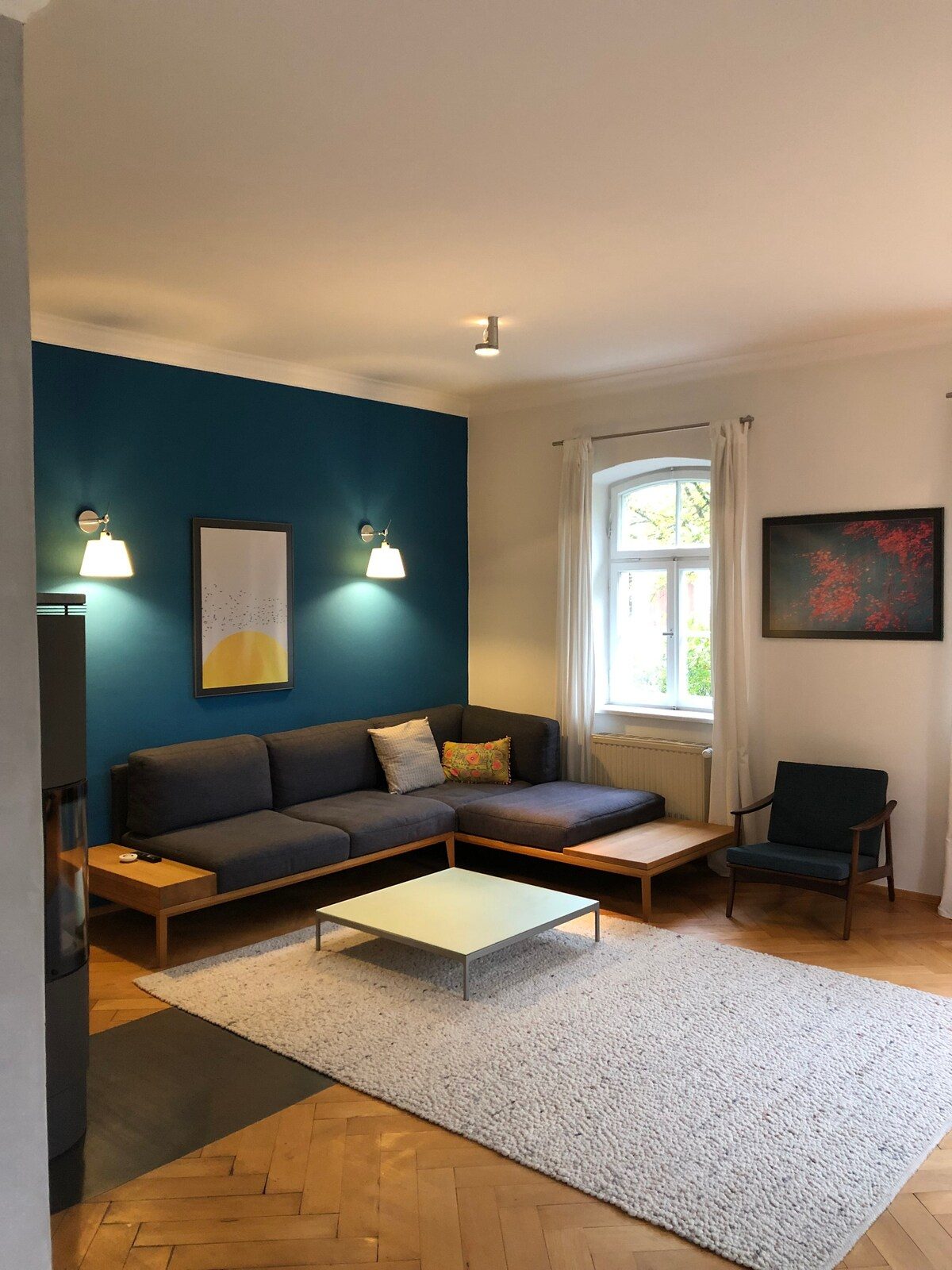 Heller Wohnraum mit hohen Decken, altem Fischgrätparkett und petrolfarbener Akzentwand.