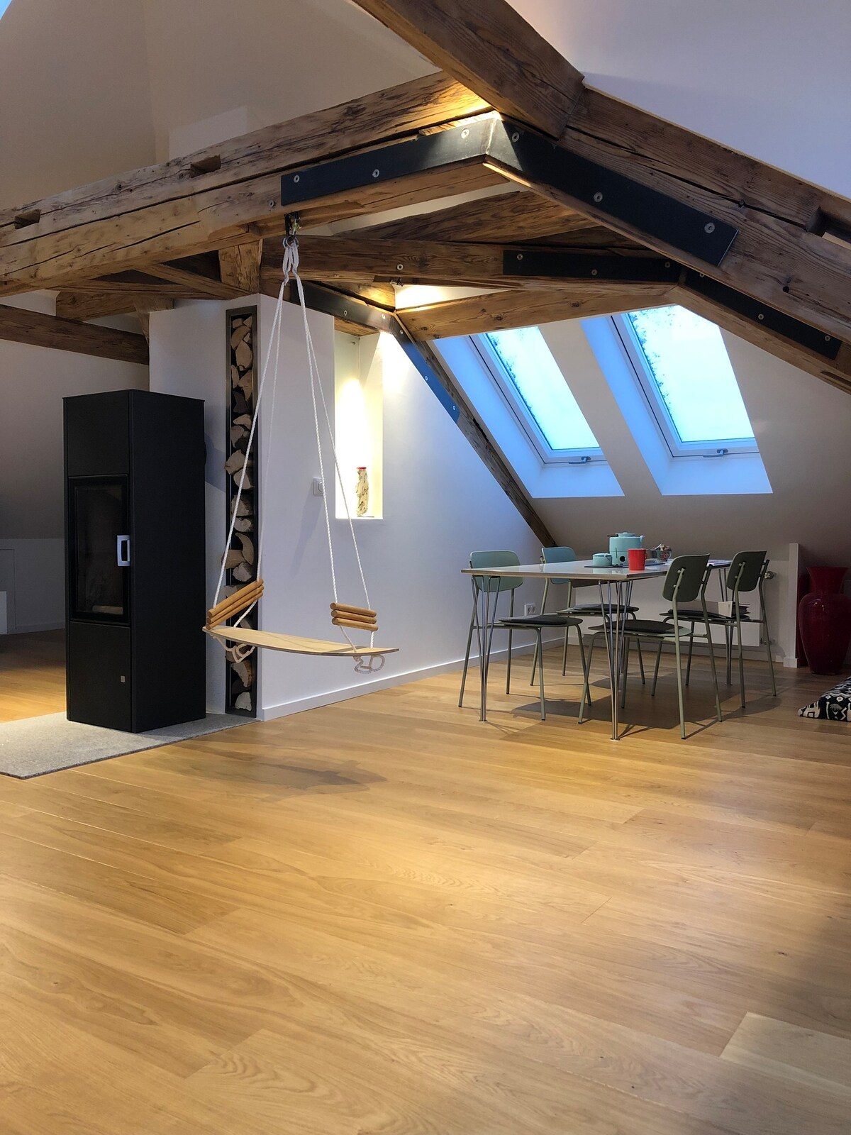 Schwarzer Schwedenofen aus Stahl neben gestapeltem Feuerholz im offenen Loft-Wohnraum.