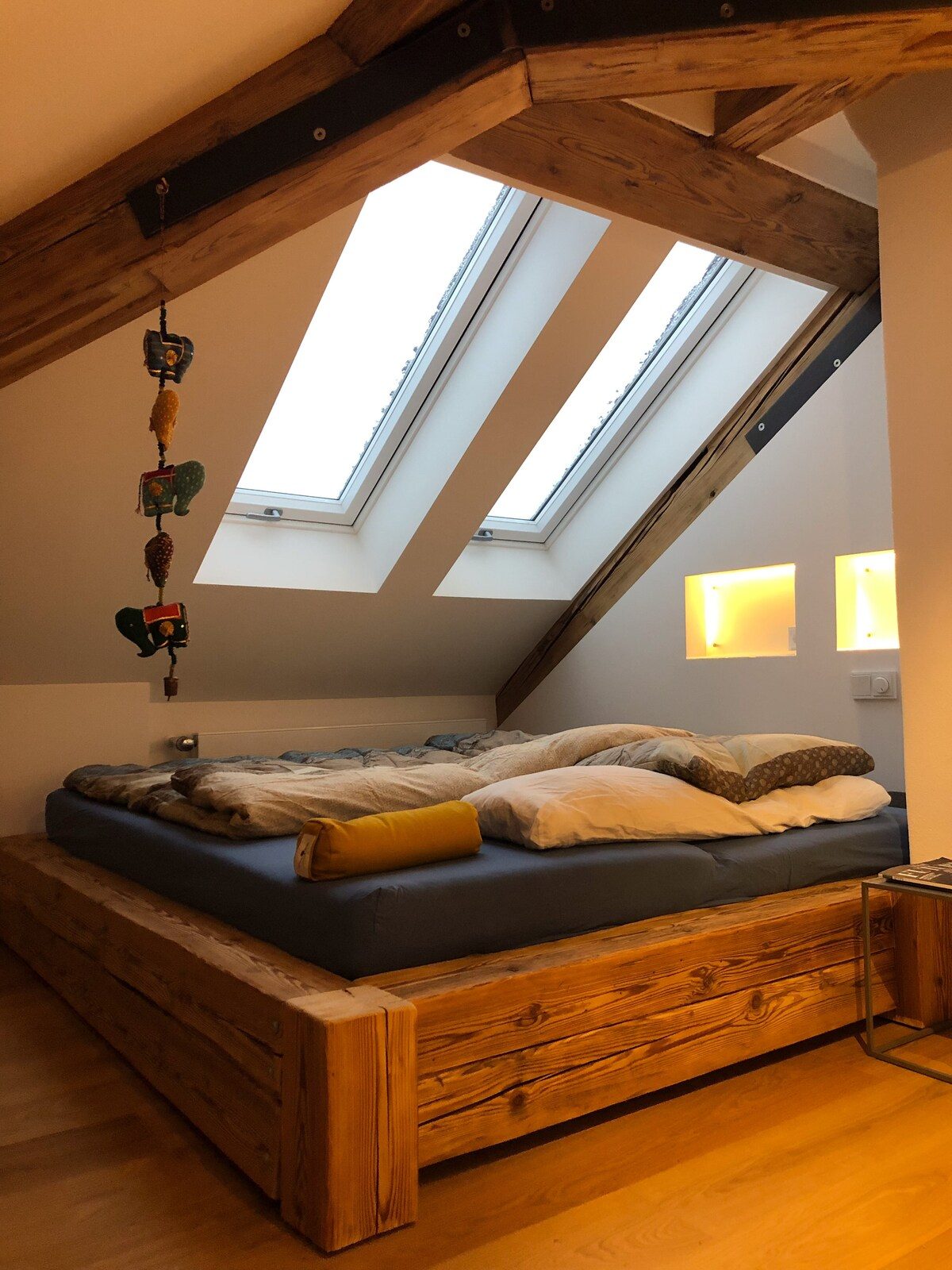 Schlafbereich des Lofts mit Massivholzbett unter zwei Dachfenstern.